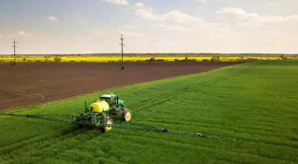 Zielony traktor z opryskiwaczem na polu, przygotowuje się do ochrony upraw przed szkodnikami, jak afalon.