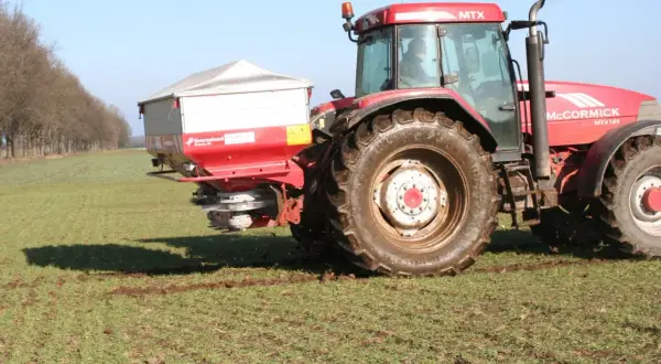 Czerwony traktor McCormick z rozsiewaczem nawozów, przygotowujący pole do wiosennych prac. Optymalne saletra wapniowa dolistnie dawkowanie zapewni zdrowy wzrost roślin.