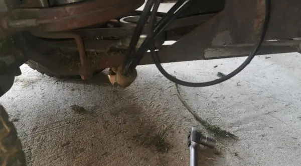 Jak założyć pasek do kosiarki traktorka Husqvarna? Widok mechanizmu napędowego z kluczem nasadowym.